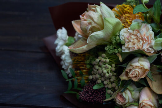 En bukett med olika blommor och gröna växter på ett mörkt underlag.